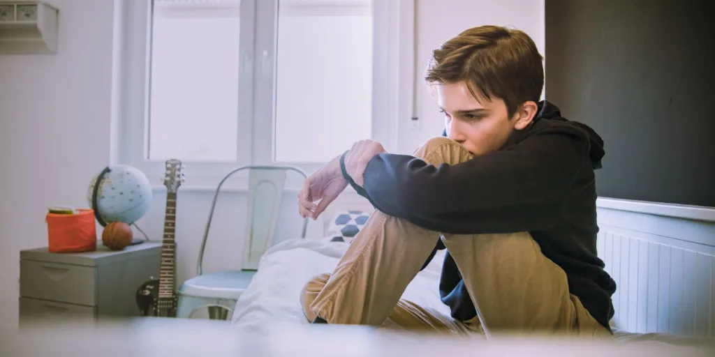 Jongen zit stil op bed en staart peinzend voor zich uit, teken van terugtrekgedrag